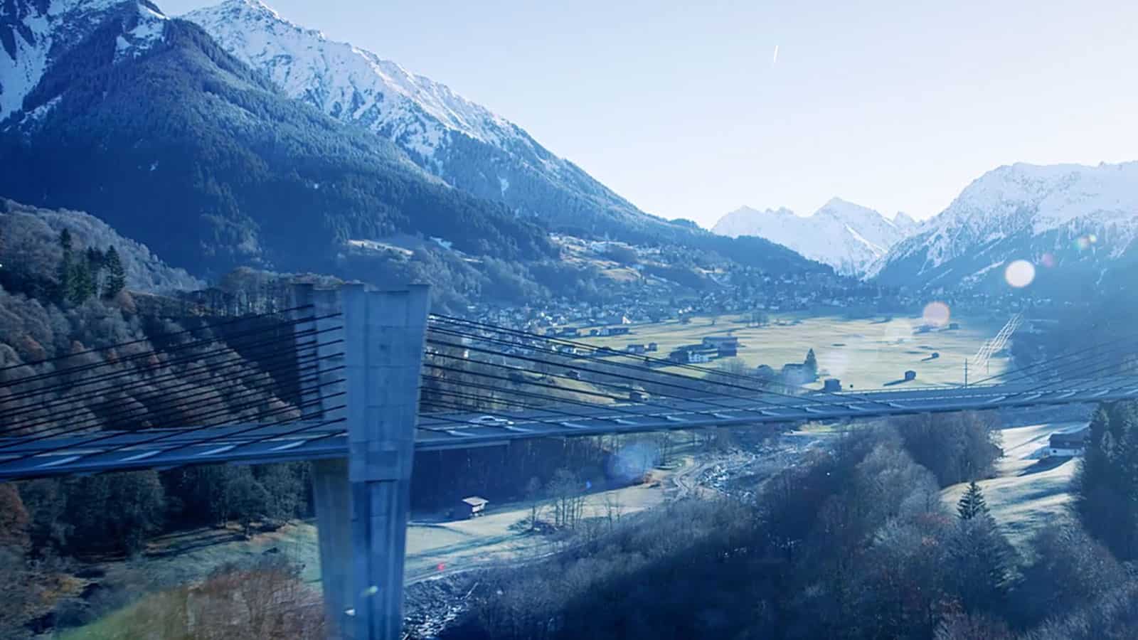 Video still of mountainous area, with bridge in the foreground.